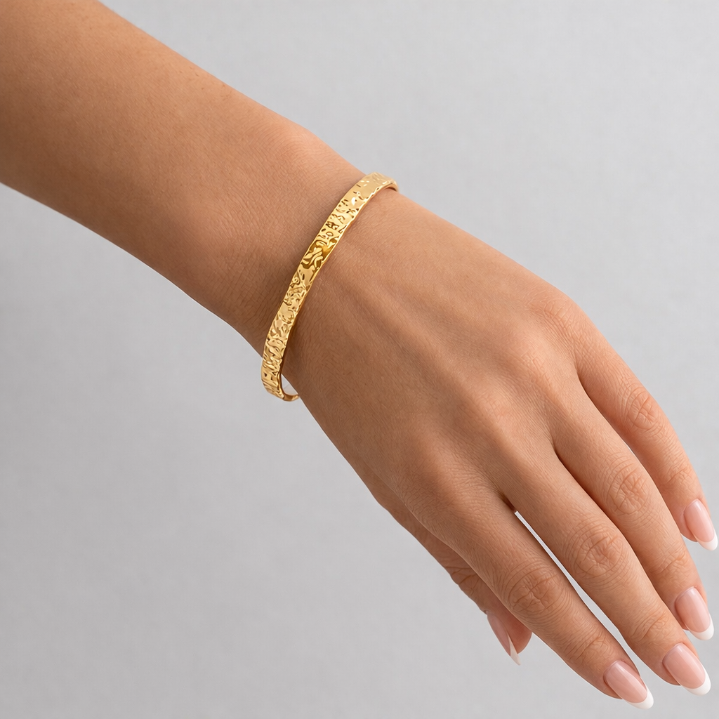 Gold bracelet on a hand against a gray background