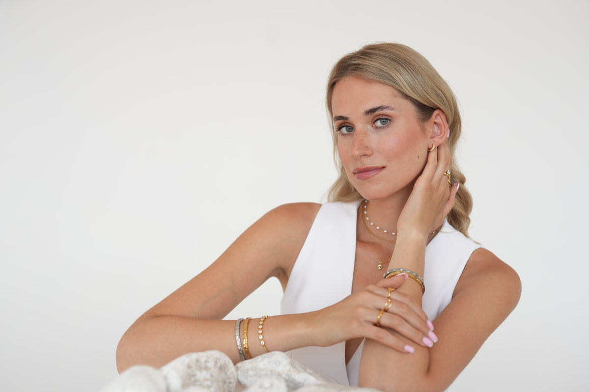 Model wearing layered gold necklaces, gold rings and bracelets with a white waistcoat.