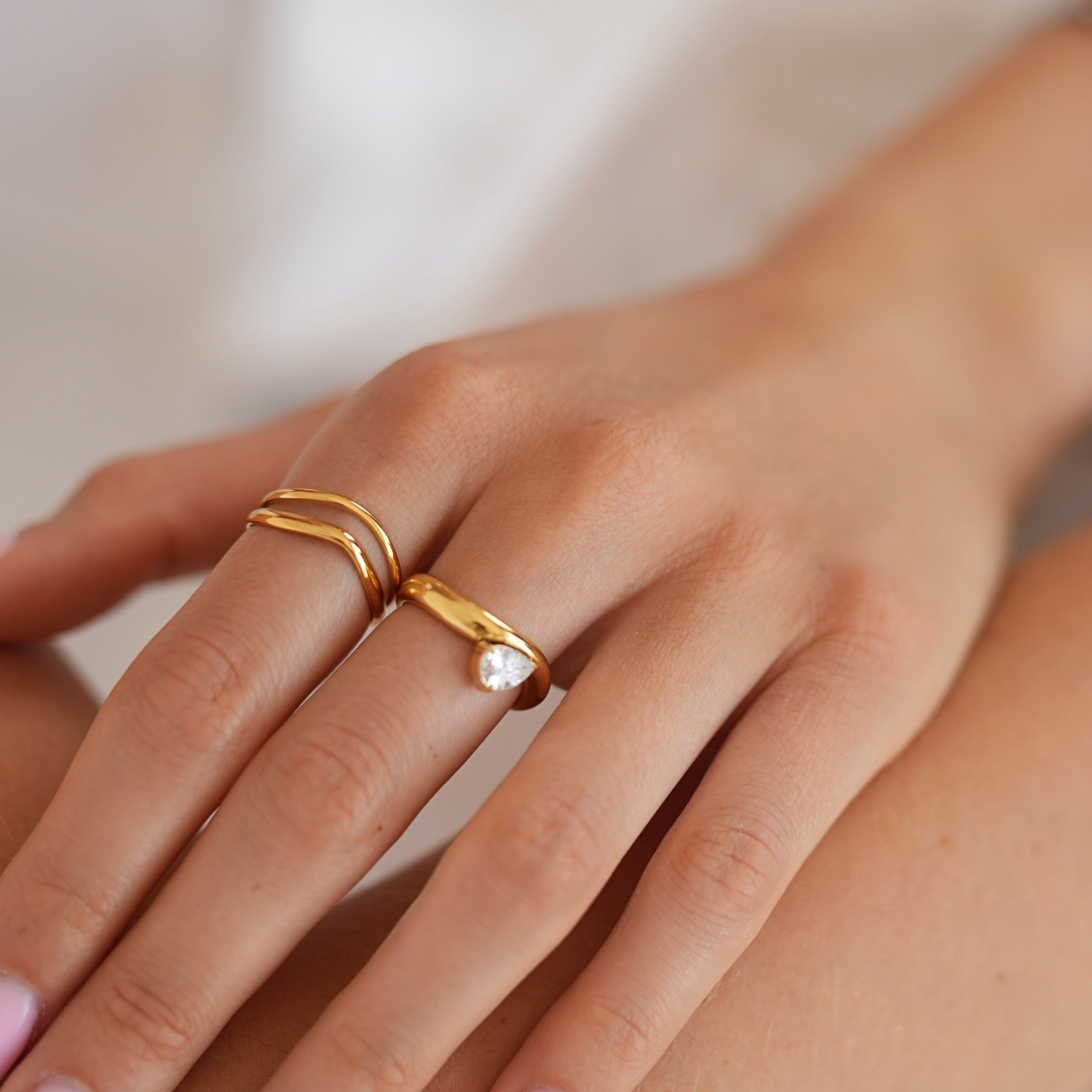 A close-up of a person's hands and wrists wearing multiple gold rings and bracelets, with a small pearl accent on one ring.