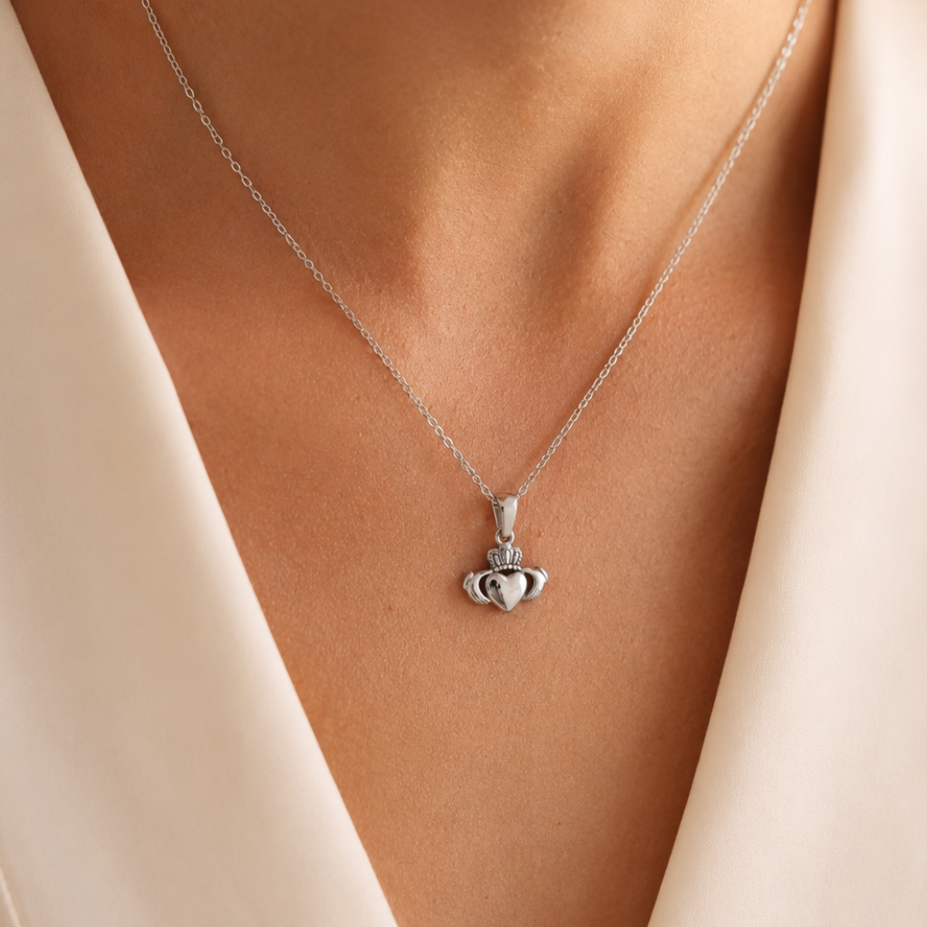 Silver claddagh pendant necklace on a person wearing a beige top.